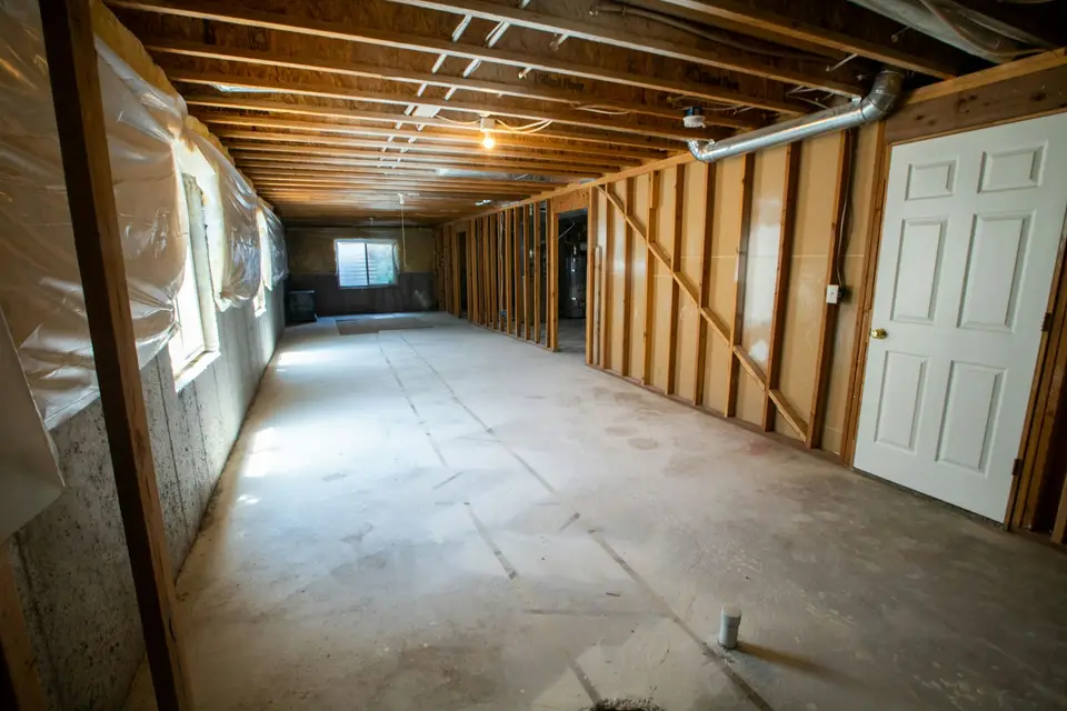 Technician in protective suit and respirator removing wet drywall from a basement after a sewage backup — Worcester, MA