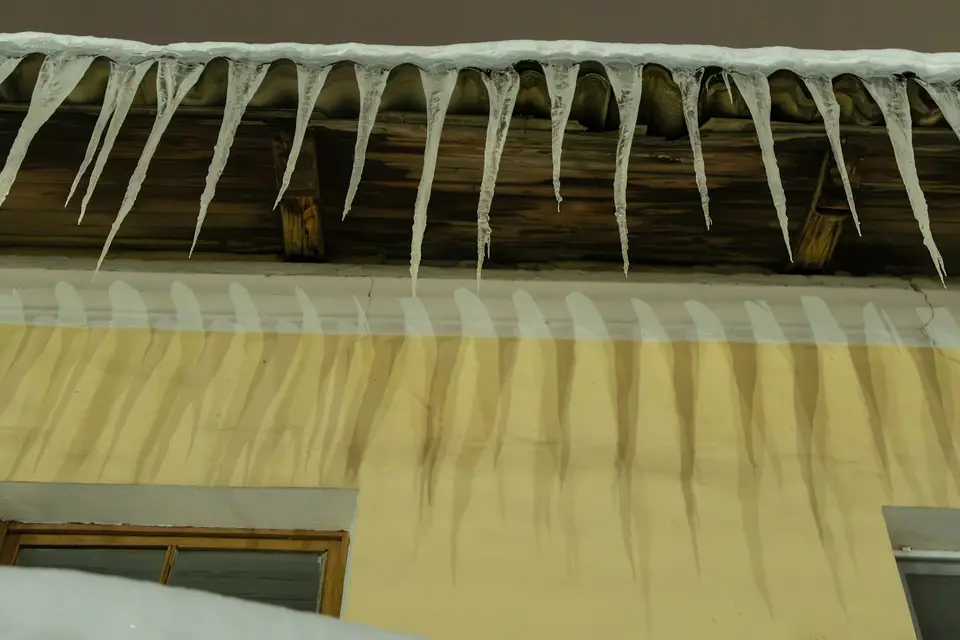 Ice dam and icicles along the eaves of a New England house, with a water stain on the ceiling inside